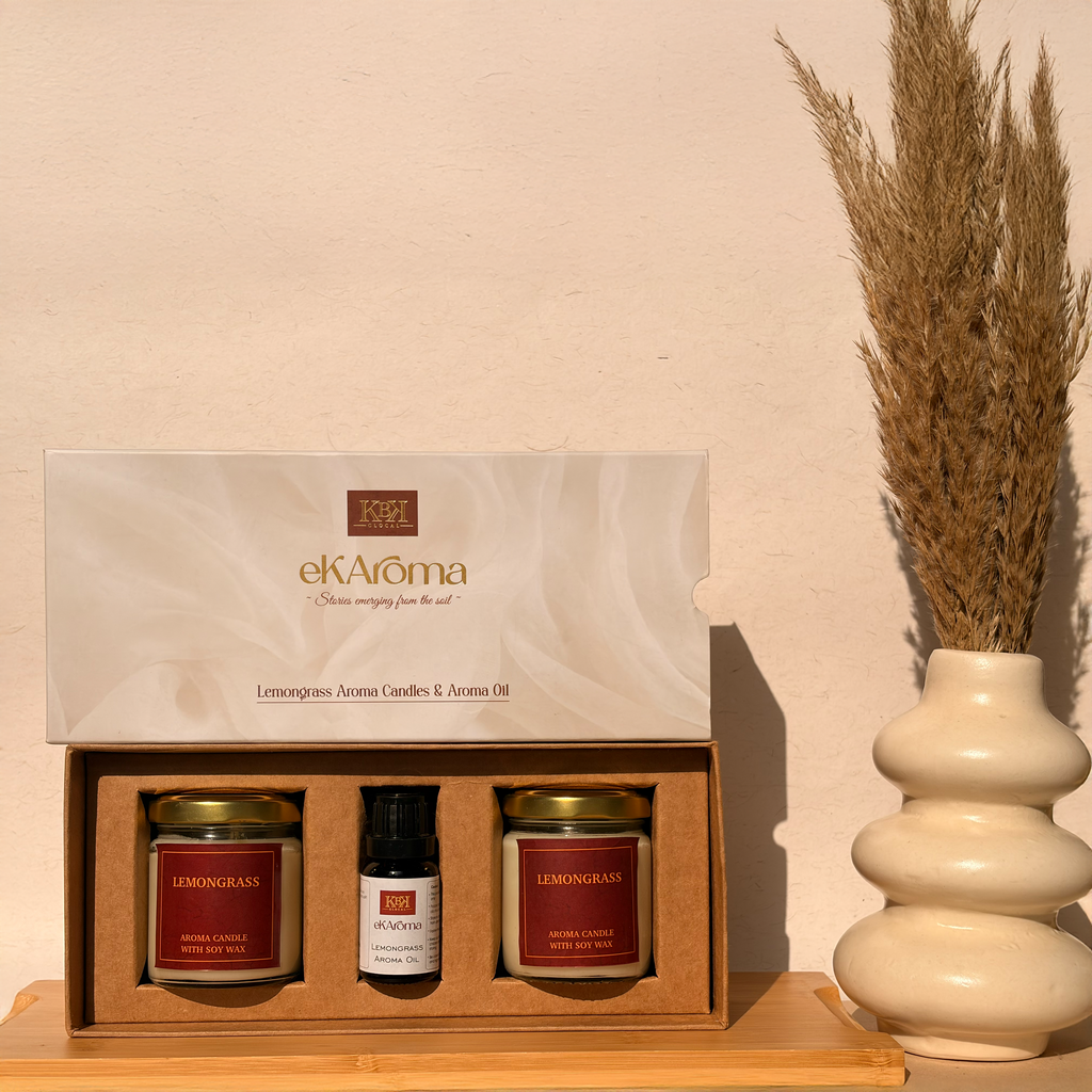 Gift set with candles and a bottle of aroma oil from ekAroma on a wooden surface with a vase in the background.
